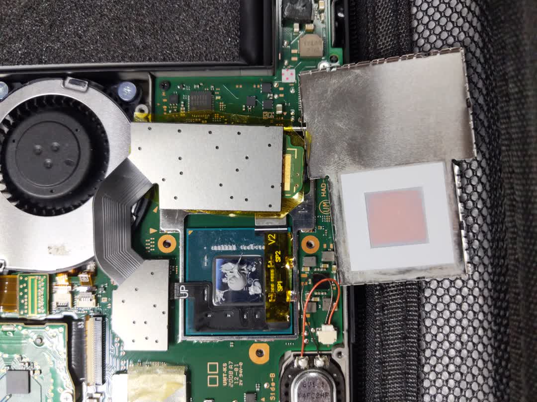 Close-up of the inside of a switch
    console. The internal heat spreader (IHS) is removed showing the bare SOC.
    Ribbon cables going from the SOC resistors to the eMMC slot and to the
    modchip can be seen